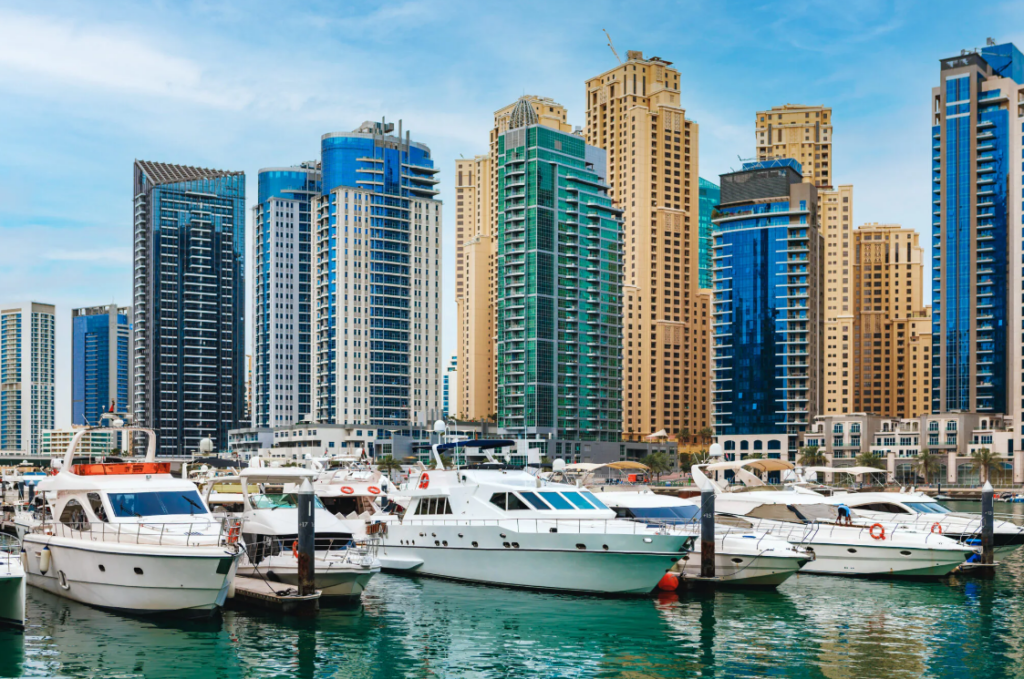 Schiffe im Hafen von Dubai. Dahinter viele Hochhäuser bei schöner Wetterlage