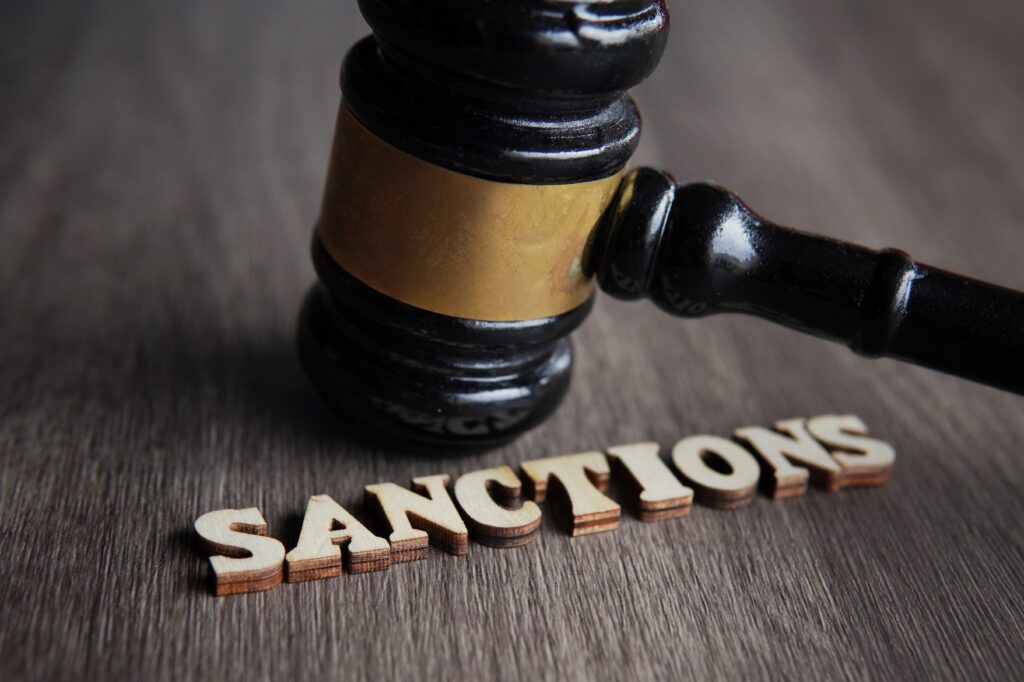 Brauner Tisch auf dem in Buchstaben Sanctions steht und ein Hammer 