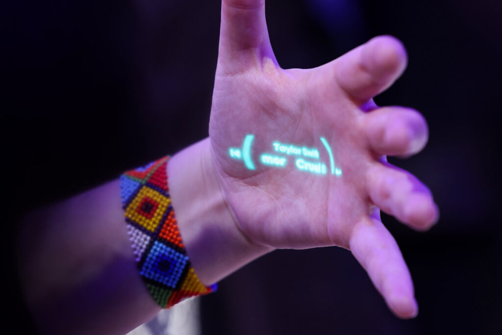 Hand mit buntem geknüpften Armband die eine Message vom AI Pin zeigt
