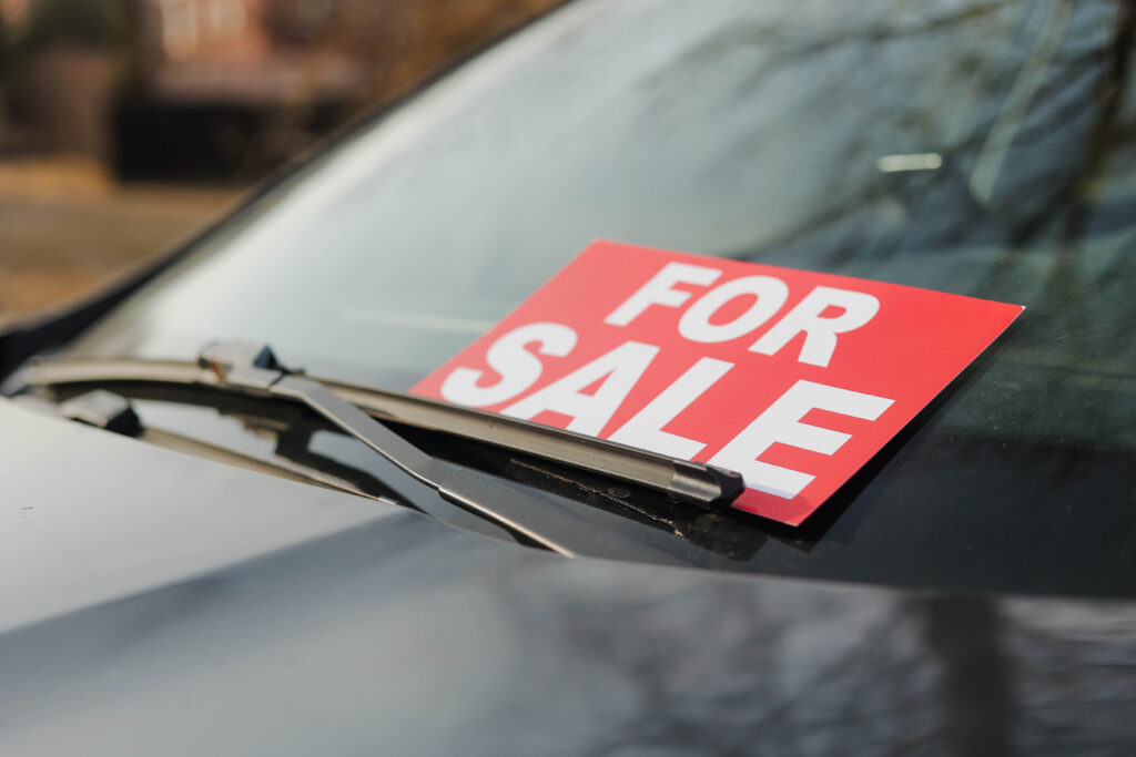 Windschutzscheibe eines Autos und ein Schild in rot mit der Aufschrift: For Sale