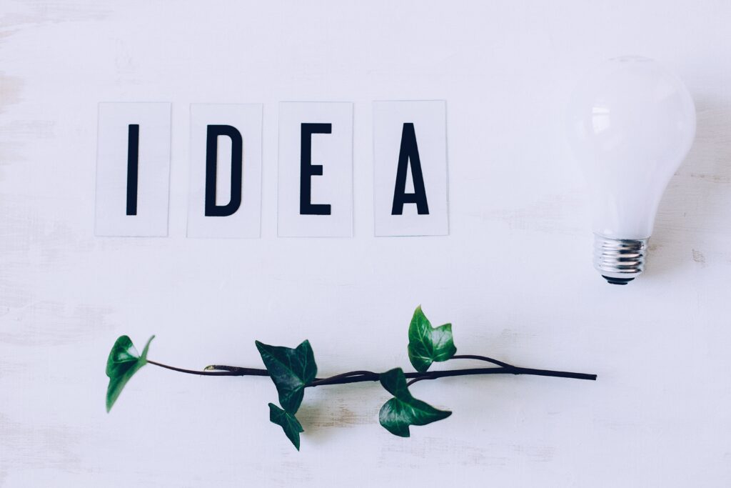 weißer Hintergrund mit den Buchstaben IDEA einer weißen Glühbirne und einem grünen Zweig