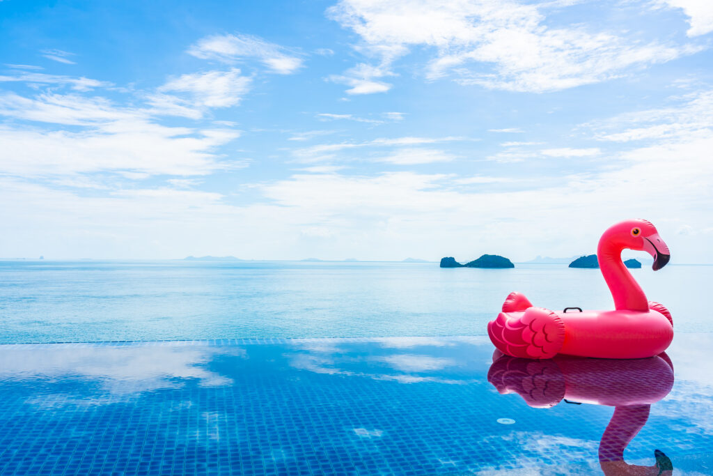 Rosaroter Plastikflamingo in einem Pool, dahinter gleich das offene Meer
