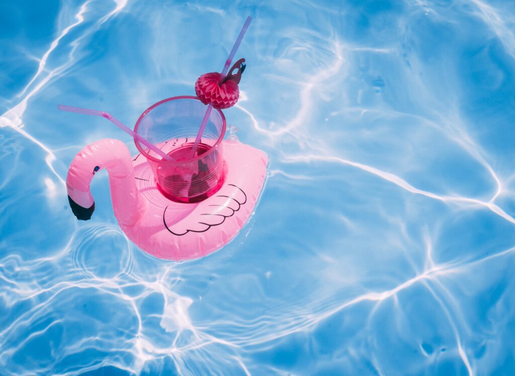 Plastikflamingo auf dem ein Cocktailglas mit Dekoration steht in einem Pool 