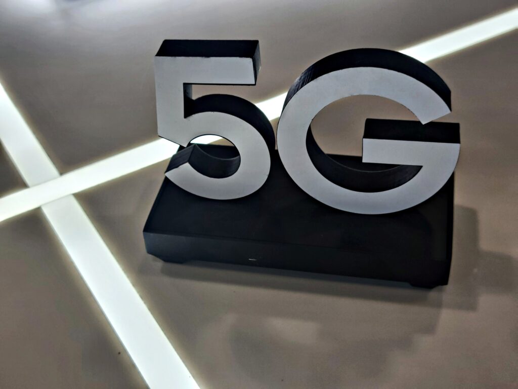 5G steht auf einem schwarzen Podest. Dahinter zwei gekreuzte Lichtstreifen