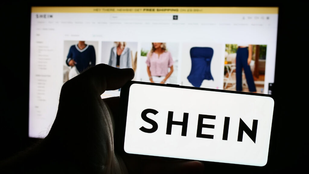 Shein wird auf einem Handy-Display angezeigt, im Hintergrund sieht man Shein-Mode auf PC