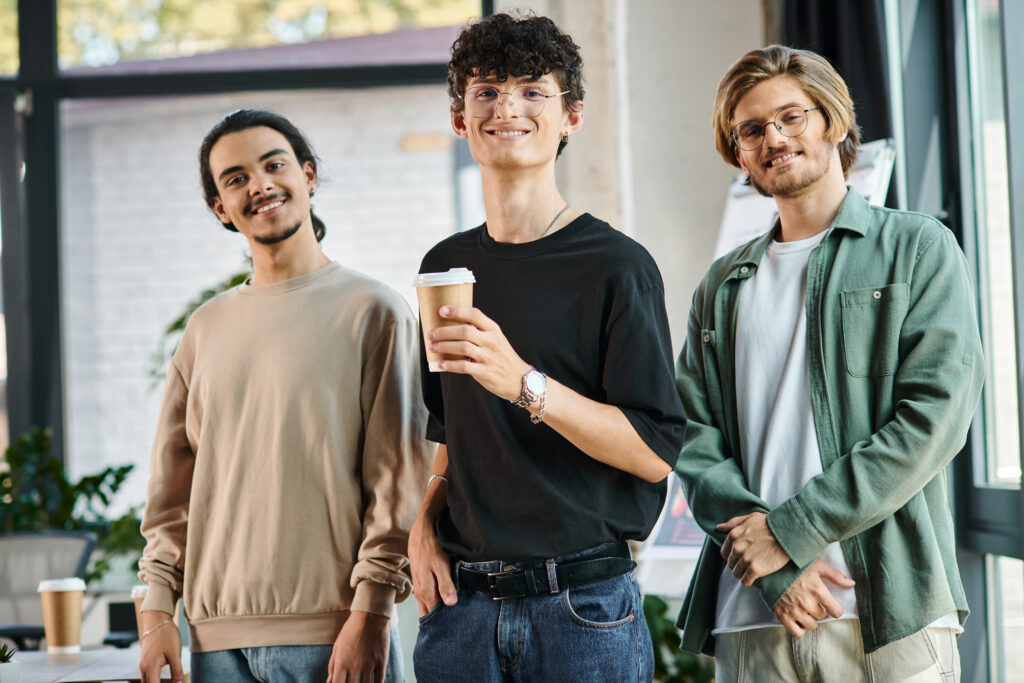 3 Junge Männer stehen nebeneinander. Einer hält einen Kaffeebecher