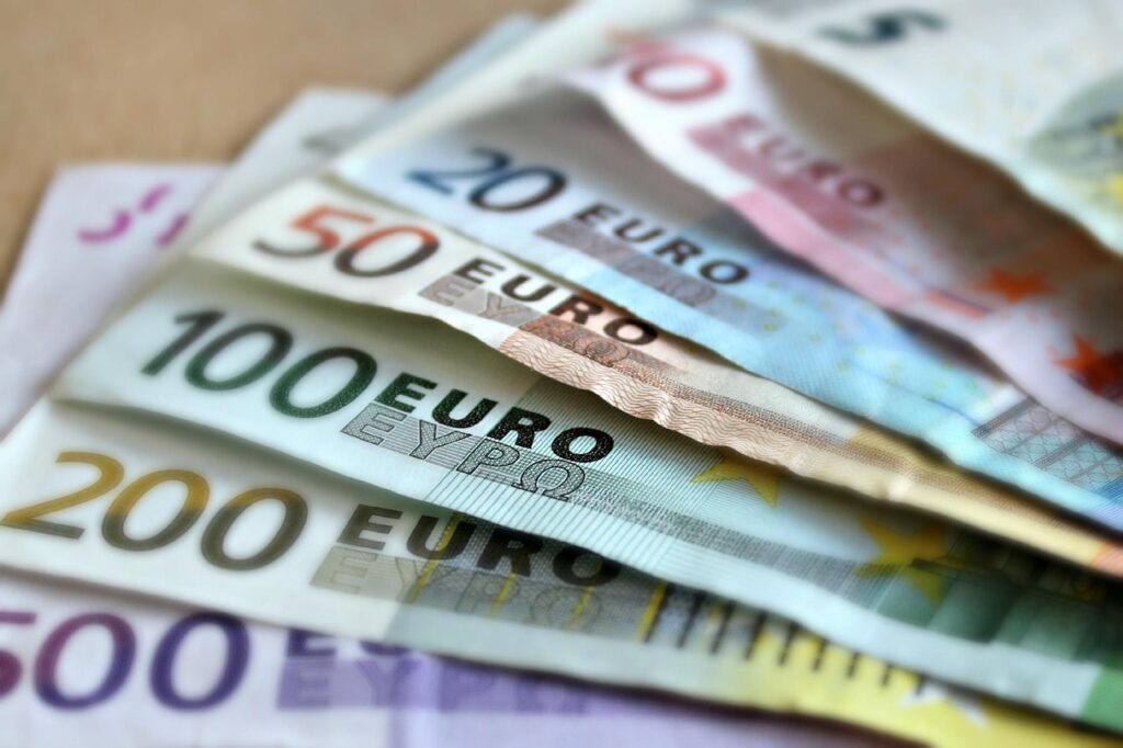 Ein Stapel Euro-Banknoten neben einer Geldbörse auf einem Holzschreibtisch symbolisiert die Frage, ab welchem Einkommen man zur Oberschicht gehört – Foto: martaposemuckel / Pixabay
