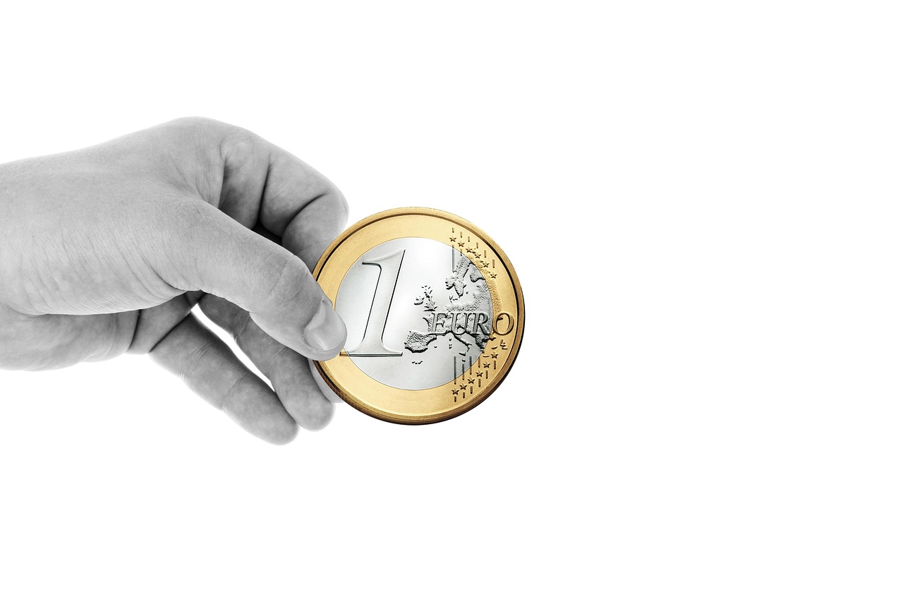 Eine Hand hält Euro-Münzen über einem Küchentisch, während im Hintergrund unscharf ein Dokument zur Mütterrente III liegt – Foto: geralt / Pixabay