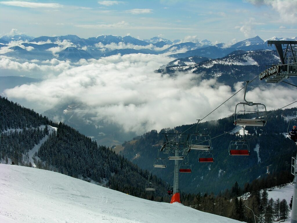 Skier und eine Pistenraupe stehen an der Talstation eines Skigebiets in Kärnten im Morgenlicht – Foto: aszak / Pixabay