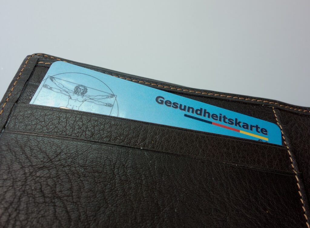 Eine Gesundheitskarte liegt neben Euromünzen auf einem Schreibtisch als Symbolbild für den steigenden Zusatzbeitrag 2026 – Foto: blickpixel / Pixabay